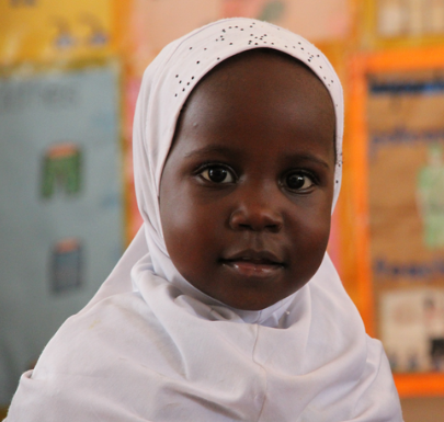 A child in a colorful outfit, smiling and sitting on a hospital bed.